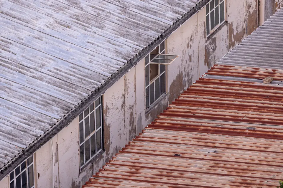 Plaques ondulées grises, usées et tachées, sur le toit d'un ancien bâtiment industriel